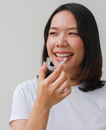 Woman smiling while holding clear aligner