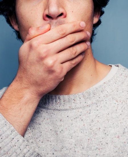 Man in need of emergency dentistry covering mouth