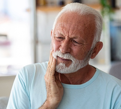 Bearded man in light blue shirt touching jaw in concern