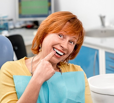 Red-haired dental patient pointing to her smile
