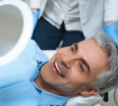 Man with veneers smiling at reflection in dentist's mirror