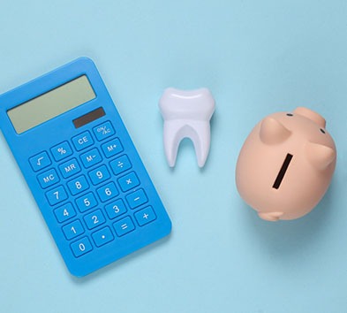A calculator, model tooth, and piggy bank against a blue background
