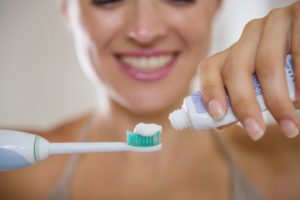 woman putting toothpaste onto an electric toothbrush 