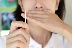 Woman holding a toothpick and covering her mouth